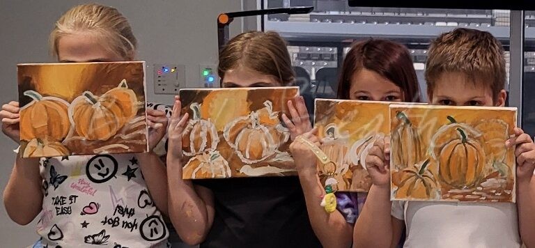 three kids holding their paintings of pumpkins