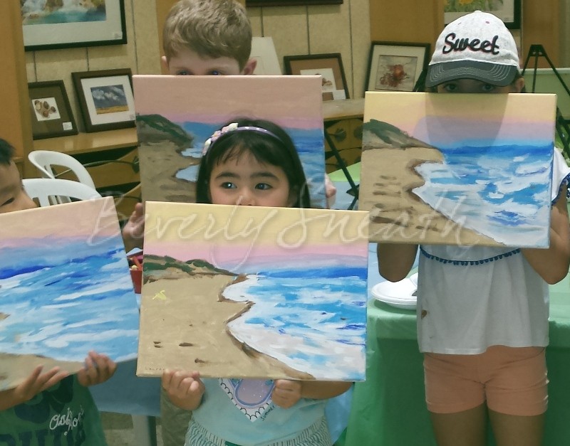 Kids holding up their paintings of a beach landscape